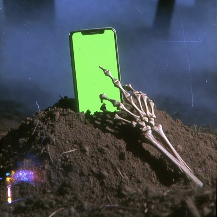 A skeleton hand reaching out of a grave holding a glowing phone